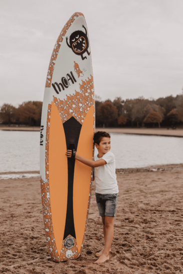 A kid on the beach holding a MOAI kid SUP board