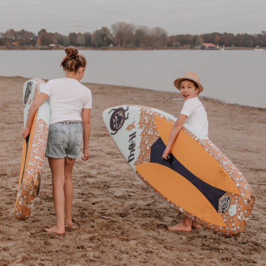 Two kids on the beach, each holding a MOAI SUP board